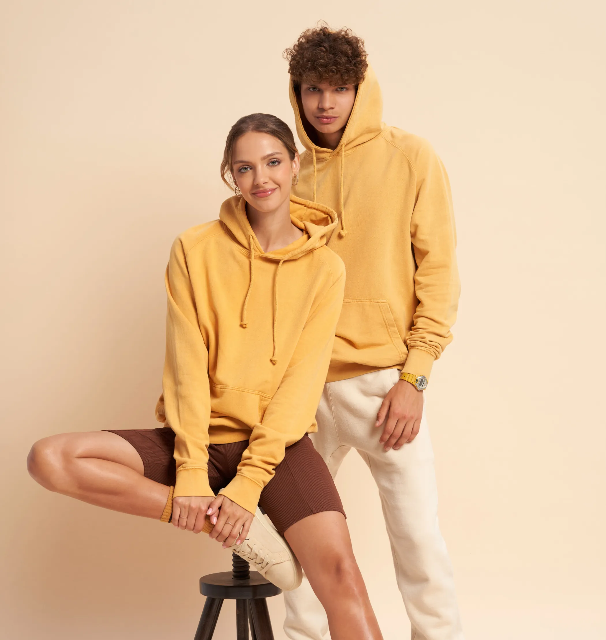 A male and a female model wearing yellow hoodies that are available to create on Fourthwall